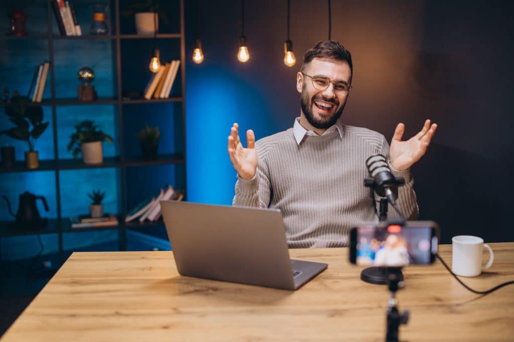 Happy male podcaster gesturing while recording audio podcast in his home studio using microphone